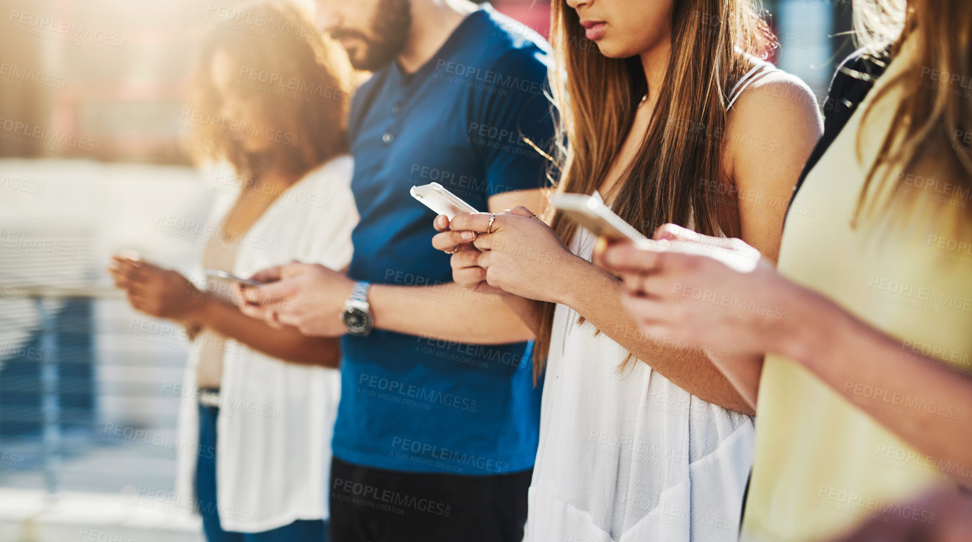 Buy stock photo Cropped shot of a group of unrecognizable young people texting on their cellphones while standing outdoors