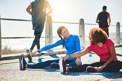 Buy stock photo Shot of two sporty young women doing warmup exercises together outdoors