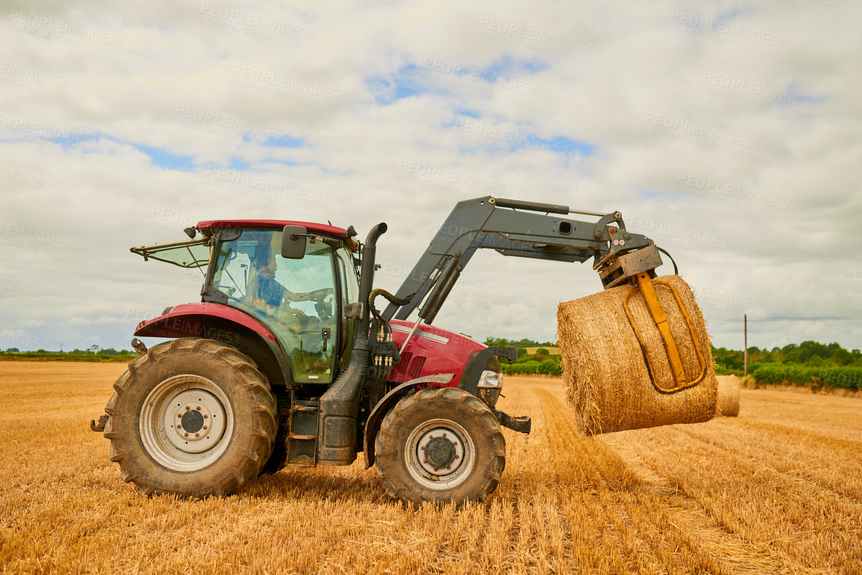 Buy stock photo Hay, agriculture and a red tractor on a farm for sustainability outdoor on an open field during the harvest season. Nature, sky and clouds with an agricultural vehicle harvesting in the countryside