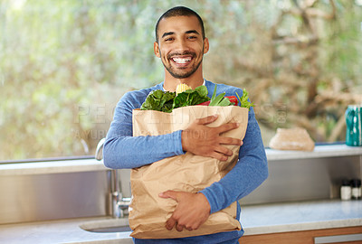 Buy stock photo Cropped portrait of a handsome young man standing in the kitchen with his groceries