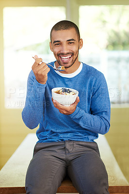 Buy stock photo Portrait of a handsome young man eating breakfast in his kitchen