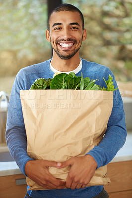 Buy stock photo Cropped portrait of a handsome young man standing in the kitchen with his groceries