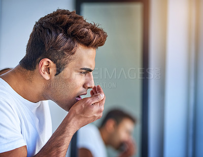 Buy stock photo Shot of a handsome young man smelling his breath during his morning grooming routine