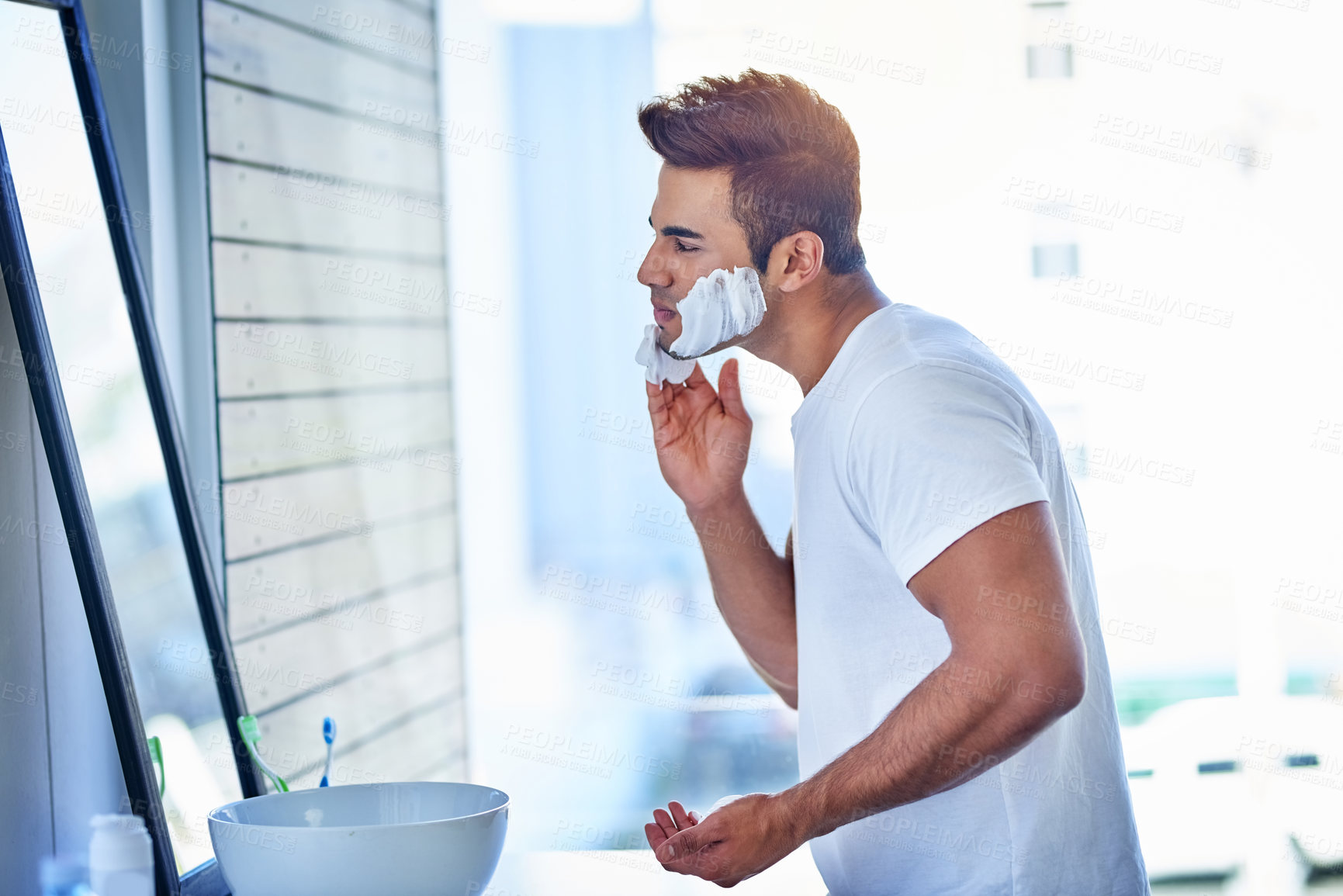 Buy stock photo Shot of a handsome young man shaving his facial hair in the bathroom