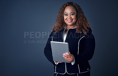 Buy stock photo Portrait of a confident young businesswoman working on her digital tablet while standing against a blue background