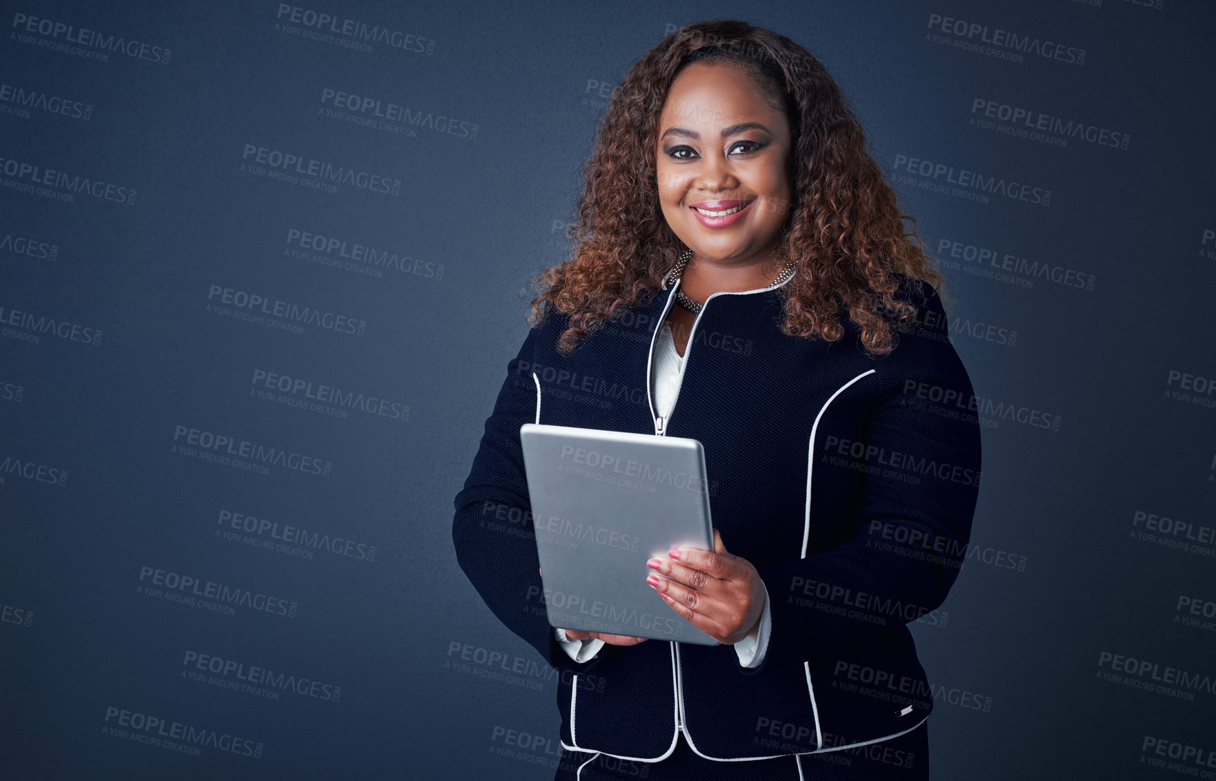 Buy stock photo Portrait of a confident young businesswoman working on her digital tablet while standing against a blue background