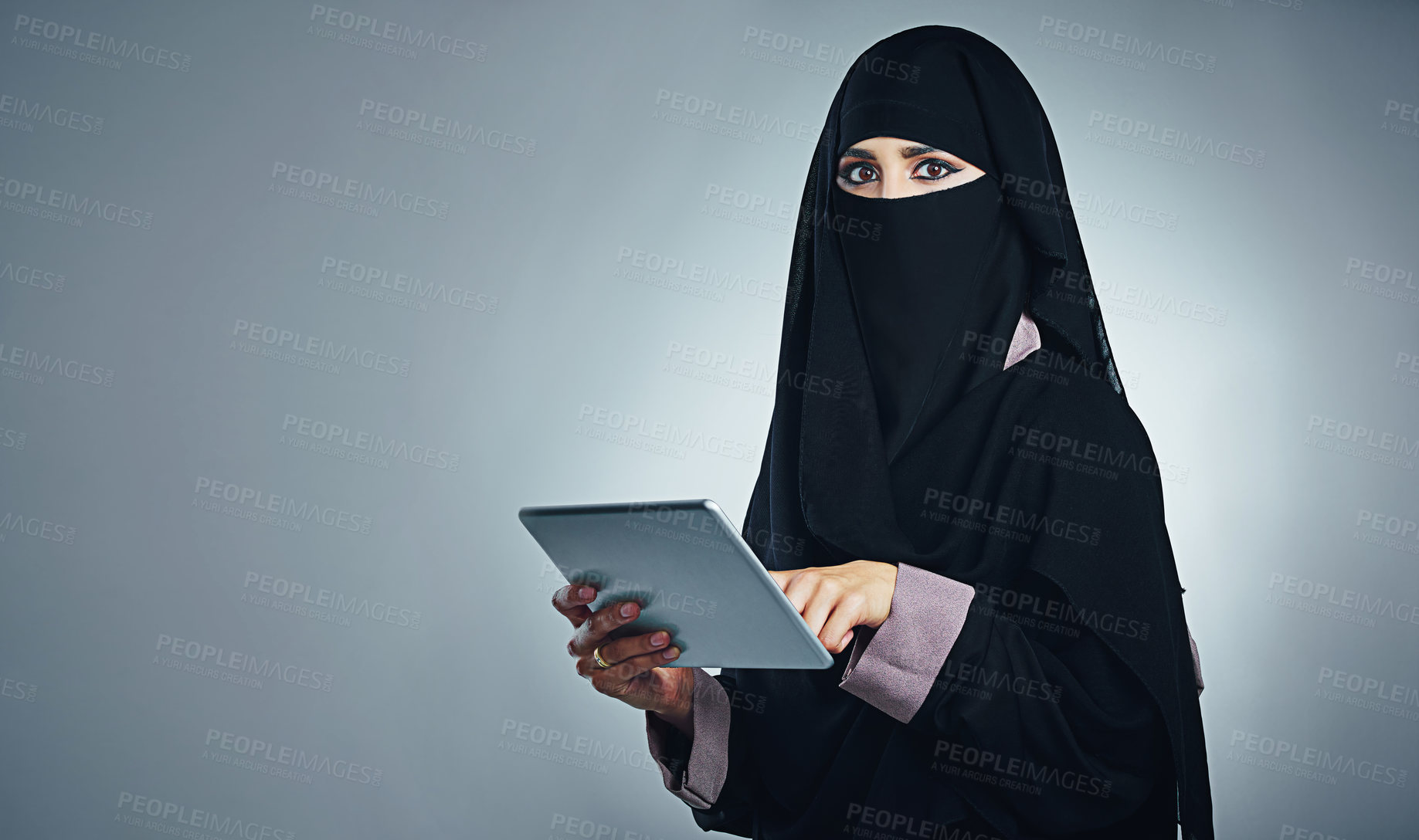 Buy stock photo Studio portrait of a young woman wearing a burqa and using a digital tablet against a gray background