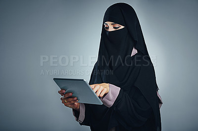 Buy stock photo Studio shot of a young woman wearing a burqa and using a digital tablet against a gray background