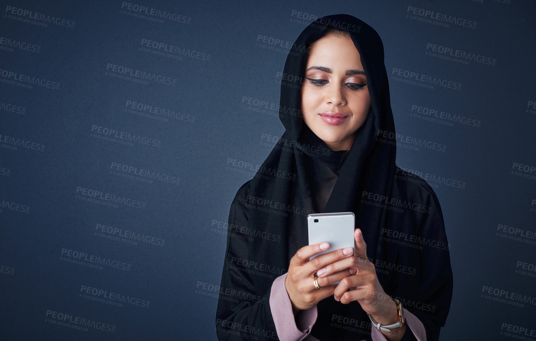 Buy stock photo Studio shot of a young woman wearing a burqa and using a mobile phone against a gray background