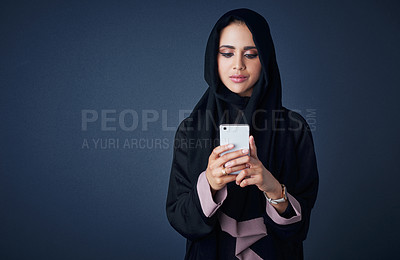 Buy stock photo Studio shot of a young woman wearing a burqa and using a mobile phone against a gray background