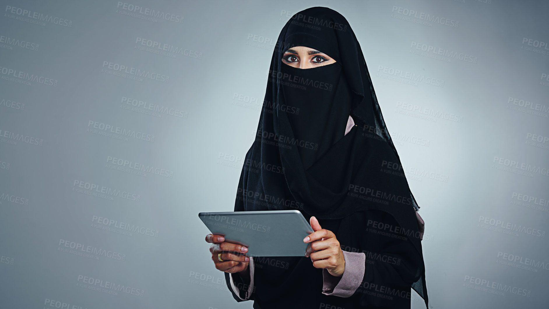Buy stock photo Studio portrait of a young woman wearing a burqa and using a digital tablet against a gray background