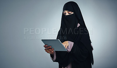 Buy stock photo Studio shot of a young woman wearing a burqa and using a digital tablet against a gray background