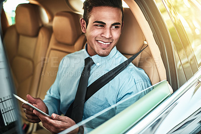Buy stock photo Shot of a young businessman using a digital tablet while sitting in the back seat of a car