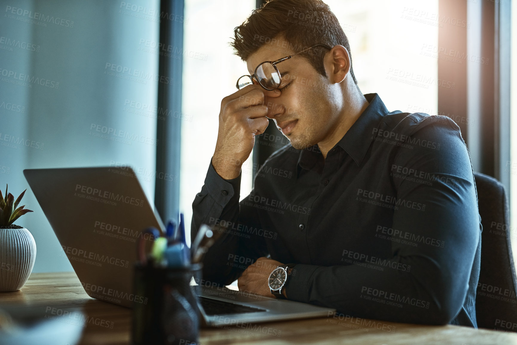 Buy stock photo Shot of a young businessman looking stressed out while working on a laptop in an office