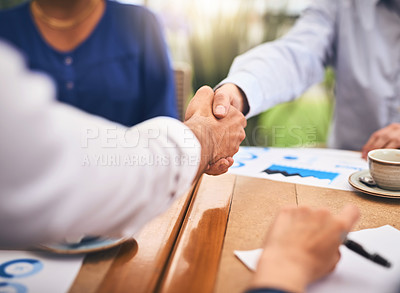 Buy stock photo Shot of two unrecognisable businesspeople shaking hands in agreement over a table at a coffeeshop
