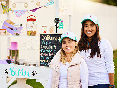 Buy stock photo Portrait of two cheerful young women standing outside together next to their baked goods stall while looking at the camera outside