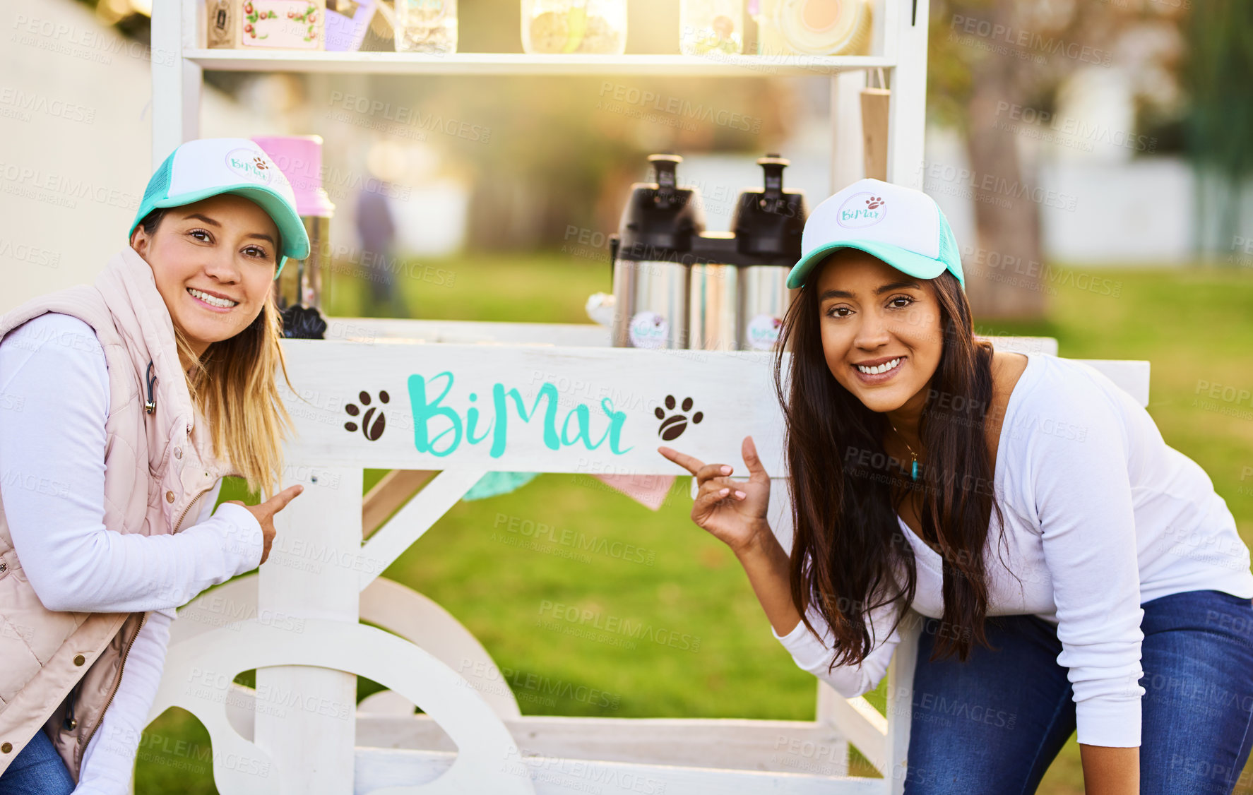 Buy stock photo Portrait of two cheerful young women standing outside together next to their baked goods stall while looking at the camera outside