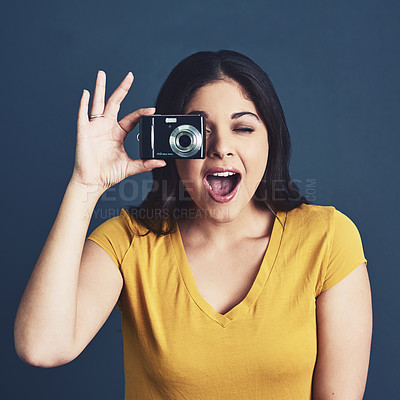 Buy stock photo Studio portrait of an attractive young woman taking a photo against a blue background