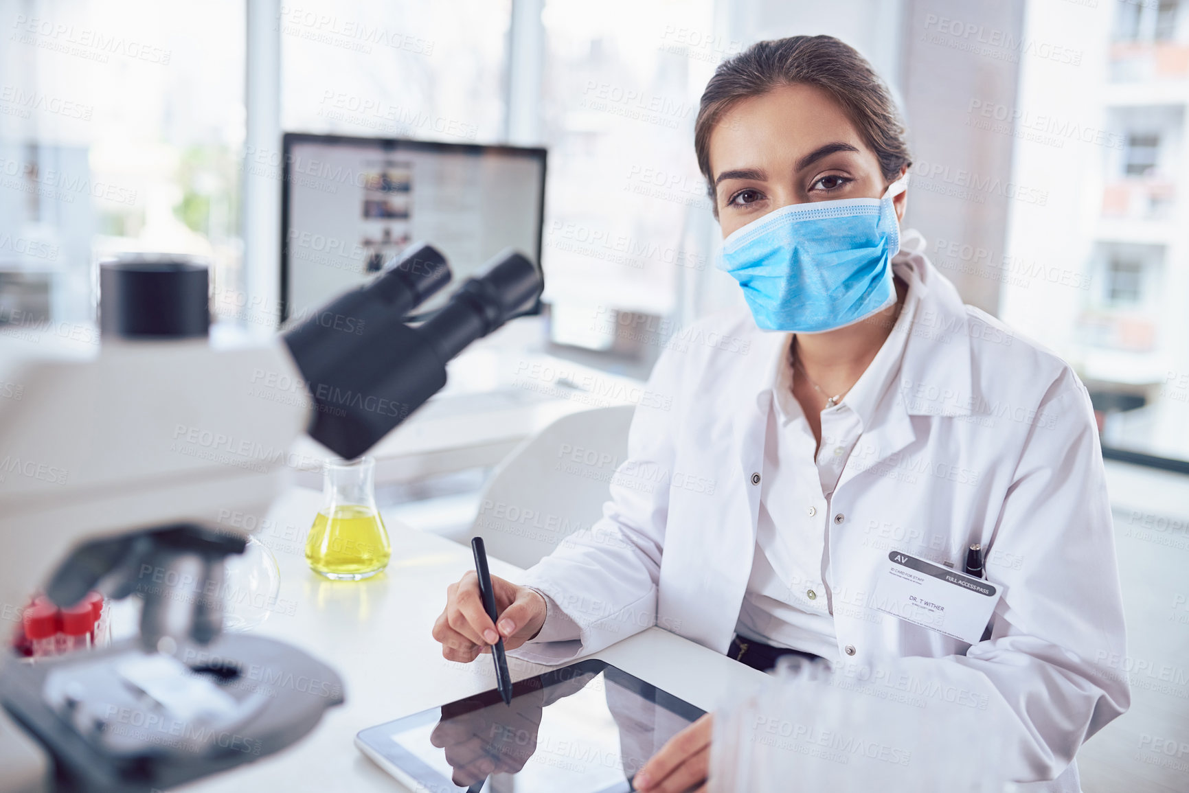 Buy stock photo Portrait of a confident young female scientist wearing a surgical mask and working on a digital tablet while looking at the camera in a laboratory