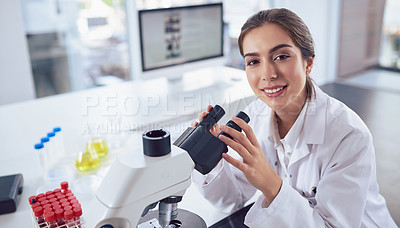 Buy stock photo Portrait of a cheerful young female scientist using a microscope while looking at the camera inside of a laboratory