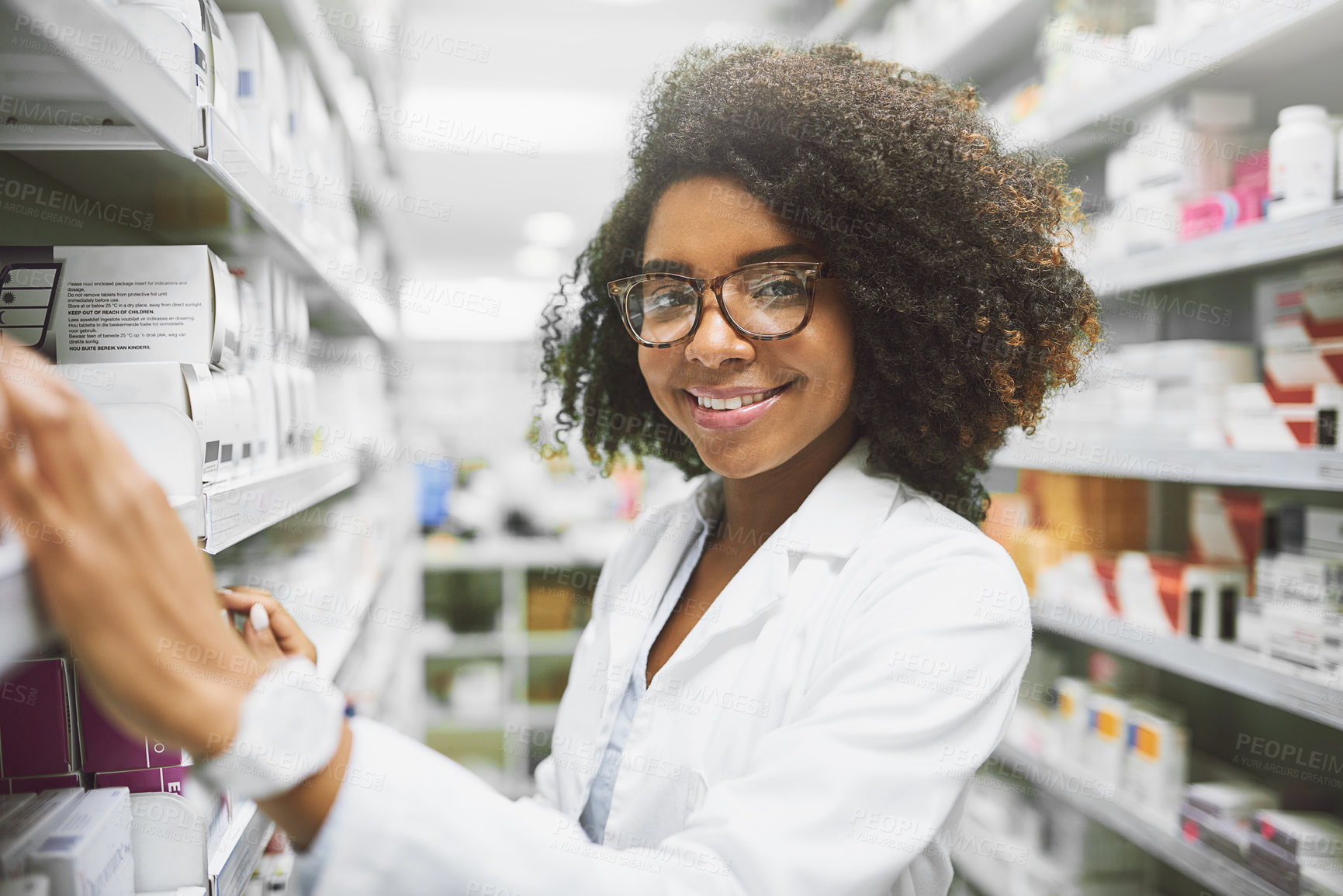 Buy stock photo Portrait of a cheerful young female pharmacist packing medication on shelves inside of a pharmacy while looking at the camera