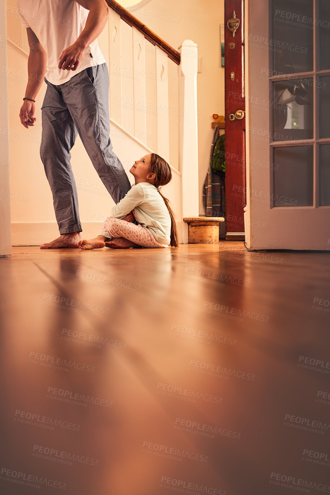 Buy stock photo Shot of a cheerful little girl grabbing hold of her dad's leg and not letting go while being seated on the ground at home