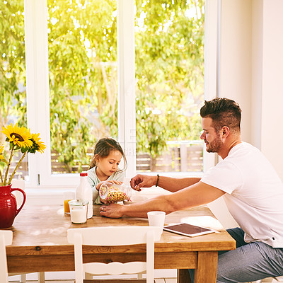 Buy stock photo Shot of a cheerful father and daughter having breakfast together while being seated around a table at home