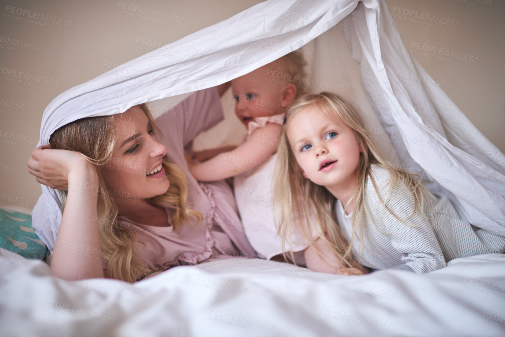 Buy stock photo Shot of an adorable family of three playing under a sheet on the bed at home