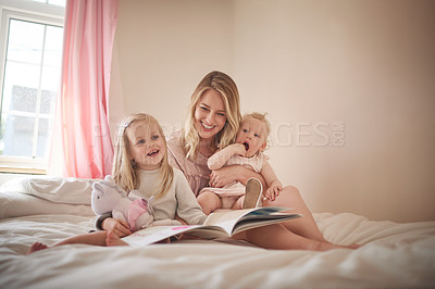 Buy stock photo Shot of an adorable family of three reading a book together on the bed at home