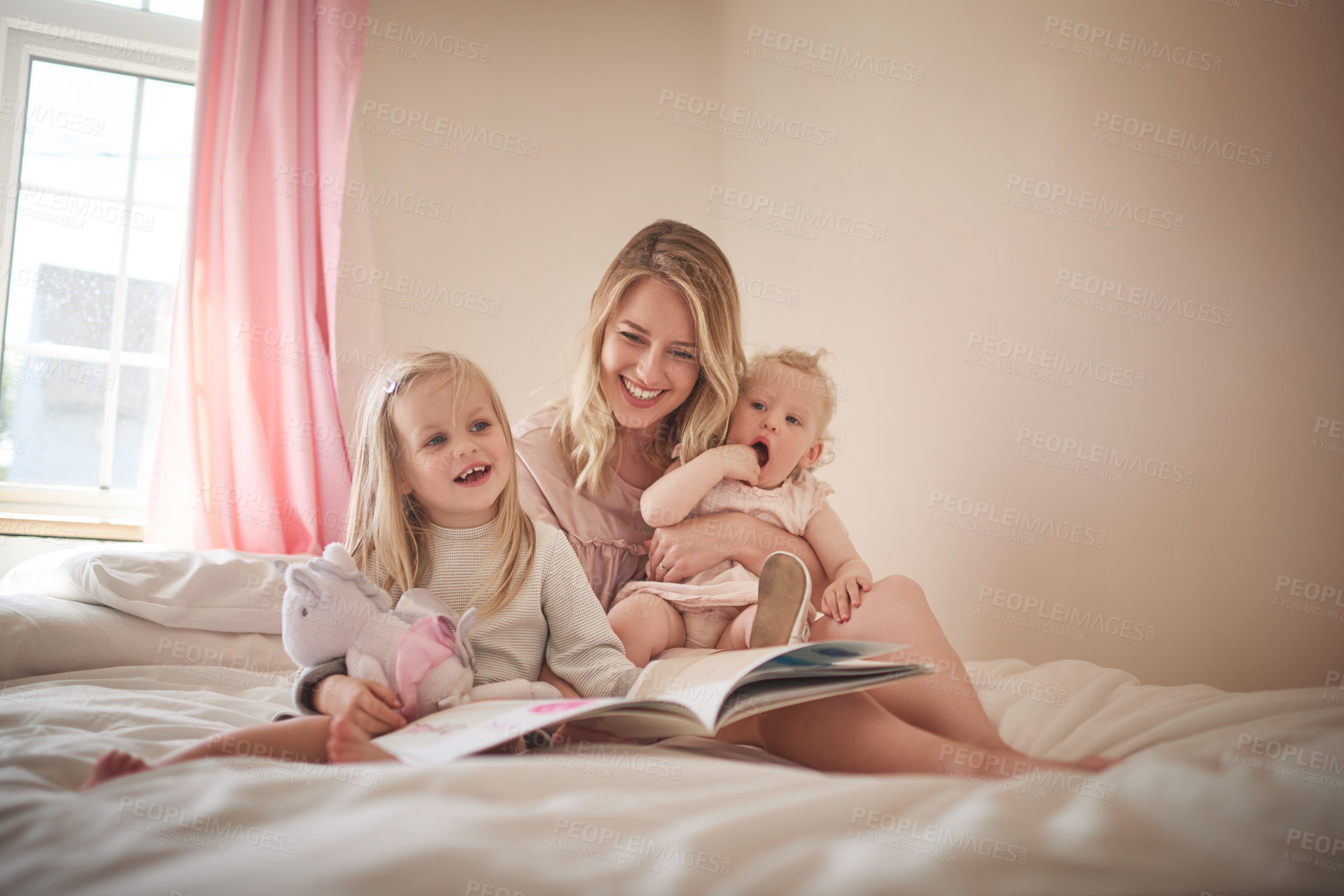 Buy stock photo Shot of an adorable family of three reading a book together on the bed at home