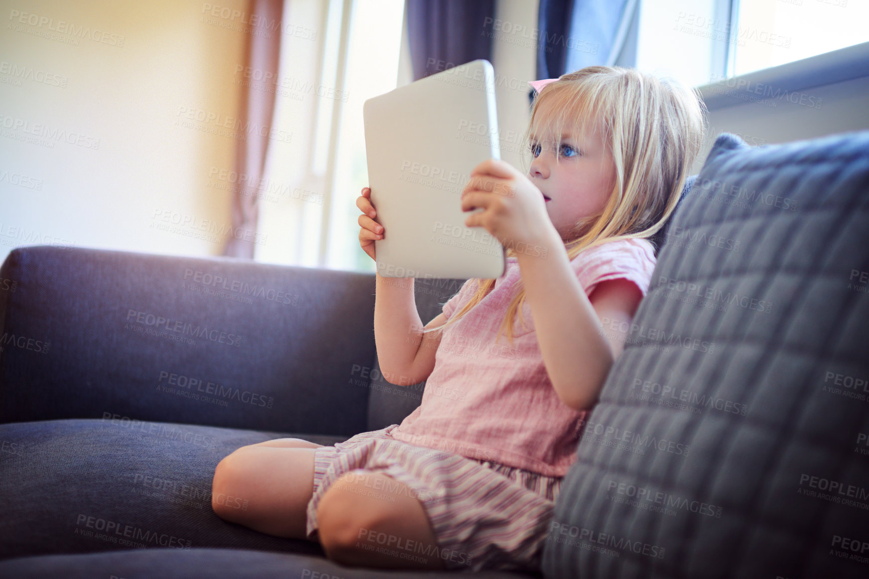 Buy stock photo Shot of an adorable little girl using a digital tablet on the sofa at home