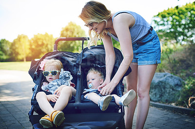 Buy stock photo Shot of a young woman putting her daughters into a pram on a day outdoors