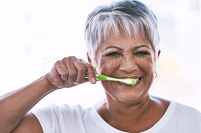 Buy stock photo Portrait of a cheerful mature woman brushing her teeth while looking at the camera at home