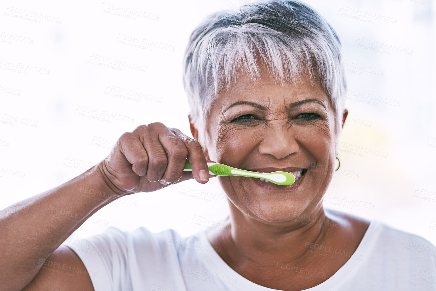 Buy stock photo Portrait of a cheerful mature woman brushing her teeth while looking at the camera at home