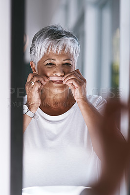 Buy stock photo Portrait of a cheerful mature woman waxing her moustache while looking into a mirror at home