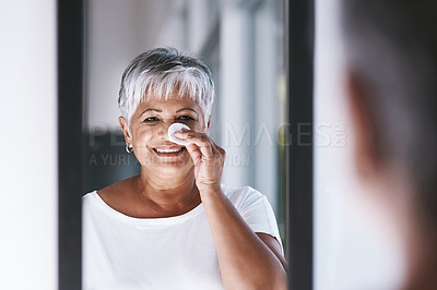 Buy stock photo Shot of a cheerful mature woman applying makeup remover on her face while looking in a mirror at home