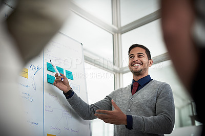 Buy stock photo Low angle shot of a young businessman explaining work related stuff during a presentation to work colleagues in a boardroom