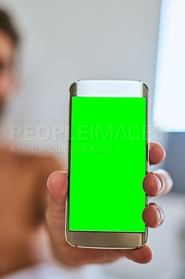Buy stock photo Shot of an unrecognizable man holding a cellphone with a green screen display at home