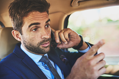 Buy stock photo Shot of a determined young businessman talking on his cellphone while being seated in the back of a car