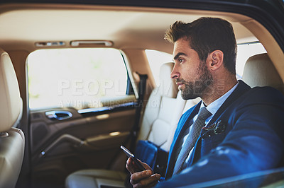 Buy stock photo Shot of a focused young businessman using his cellphone and contemplating while being seated in the back of a car