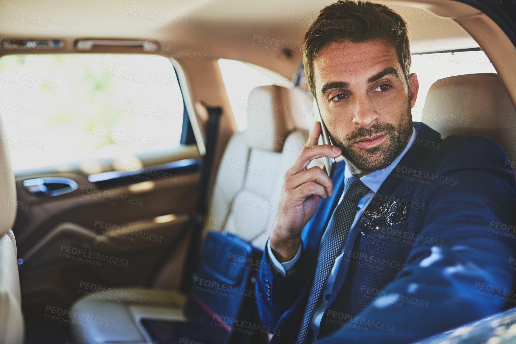 Buy stock photo Shot of a confident young businessman talking on his cellphone while being seated in the back of a car