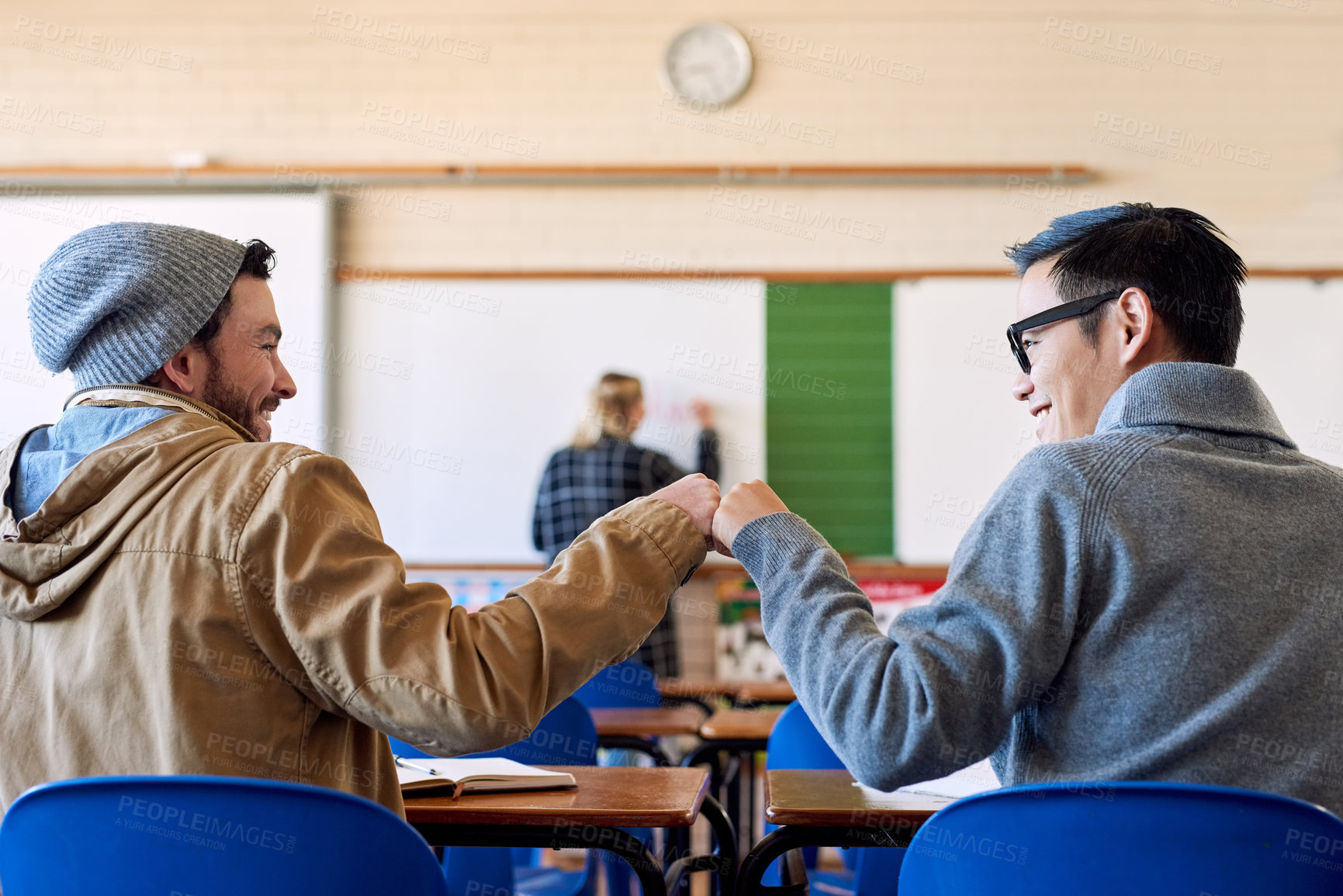 Buy stock photo Rearview shot of two young male university students fist bumping in class during a lecture