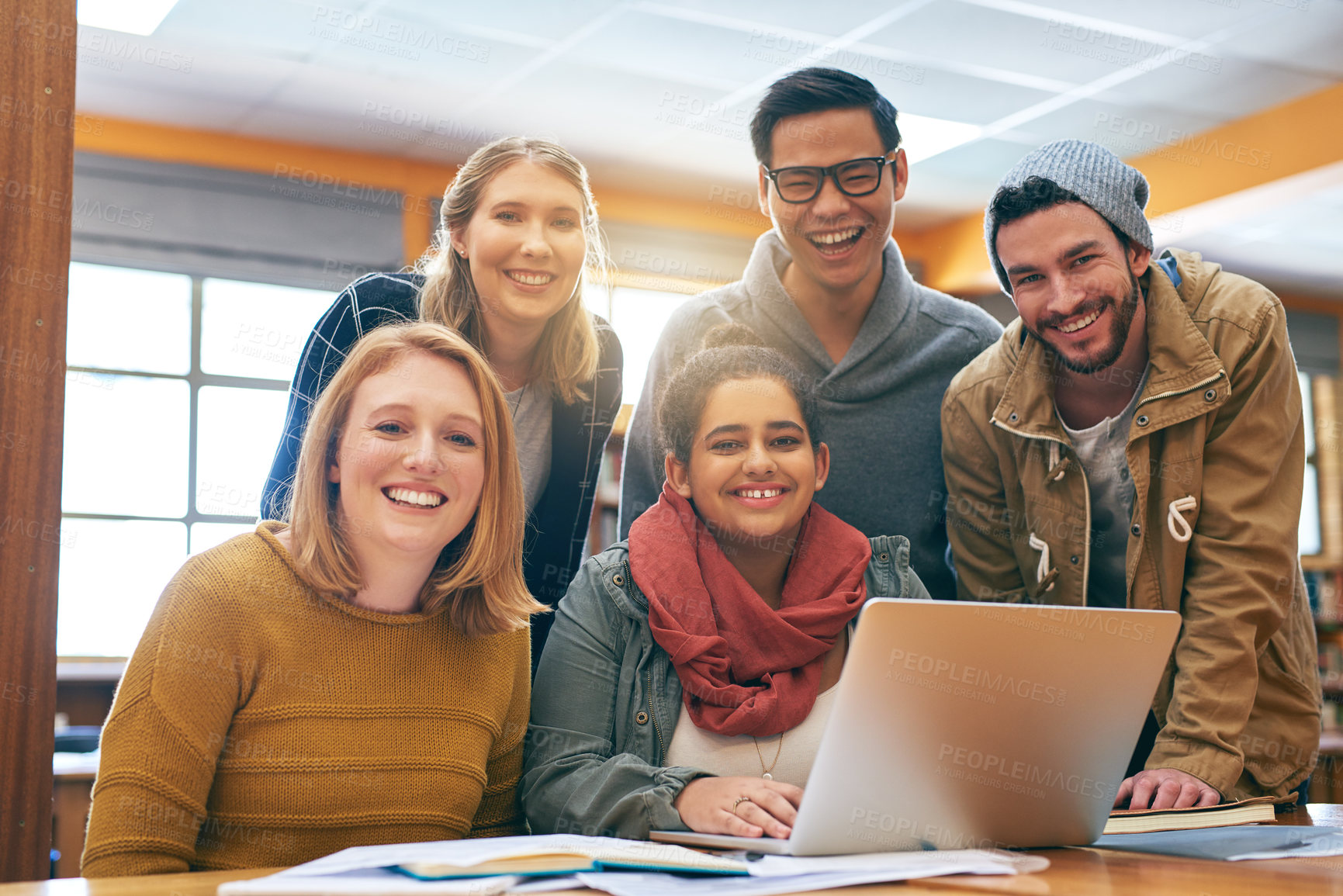 Buy stock photo Portrait of a cheerful young group of students working together using a laptop to study for exams inside of a library