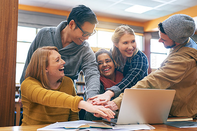 Buy stock photo Shot of a cheerful young group of students forming a huddle together while working on a laptop inside of a library