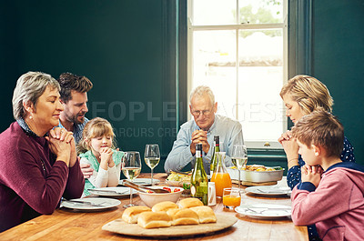 Buy stock photo Shot of a peaceful family seated around the dinner table and saying grace with eyes closed at home