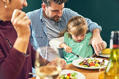 Buy stock photo Shot of a cheerful young man helping to cut his daughter's food while being seated around a dinner table at home