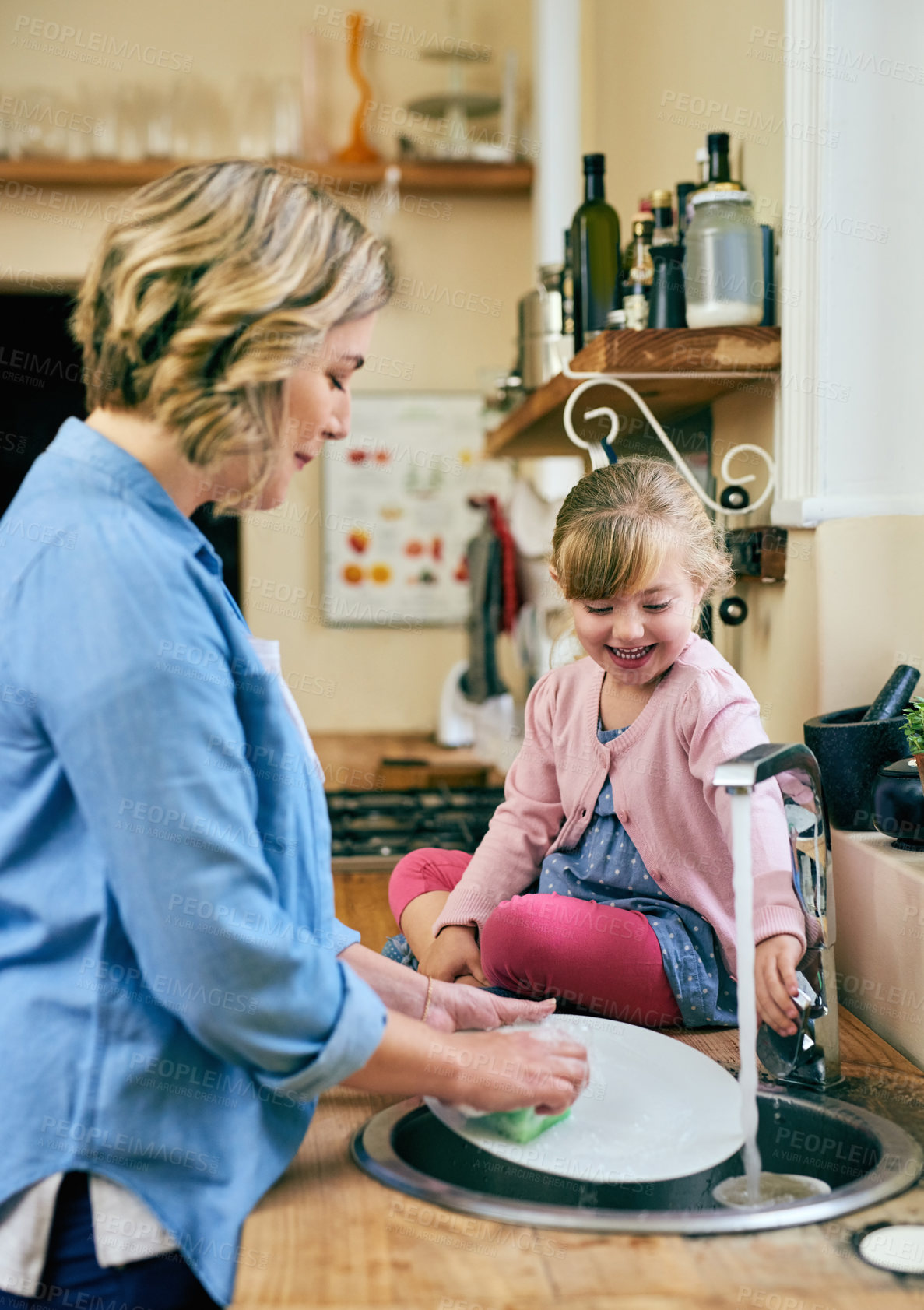 Buy stock photo Shot of a cheerful young mother and her young little daughter washing dishes together at home