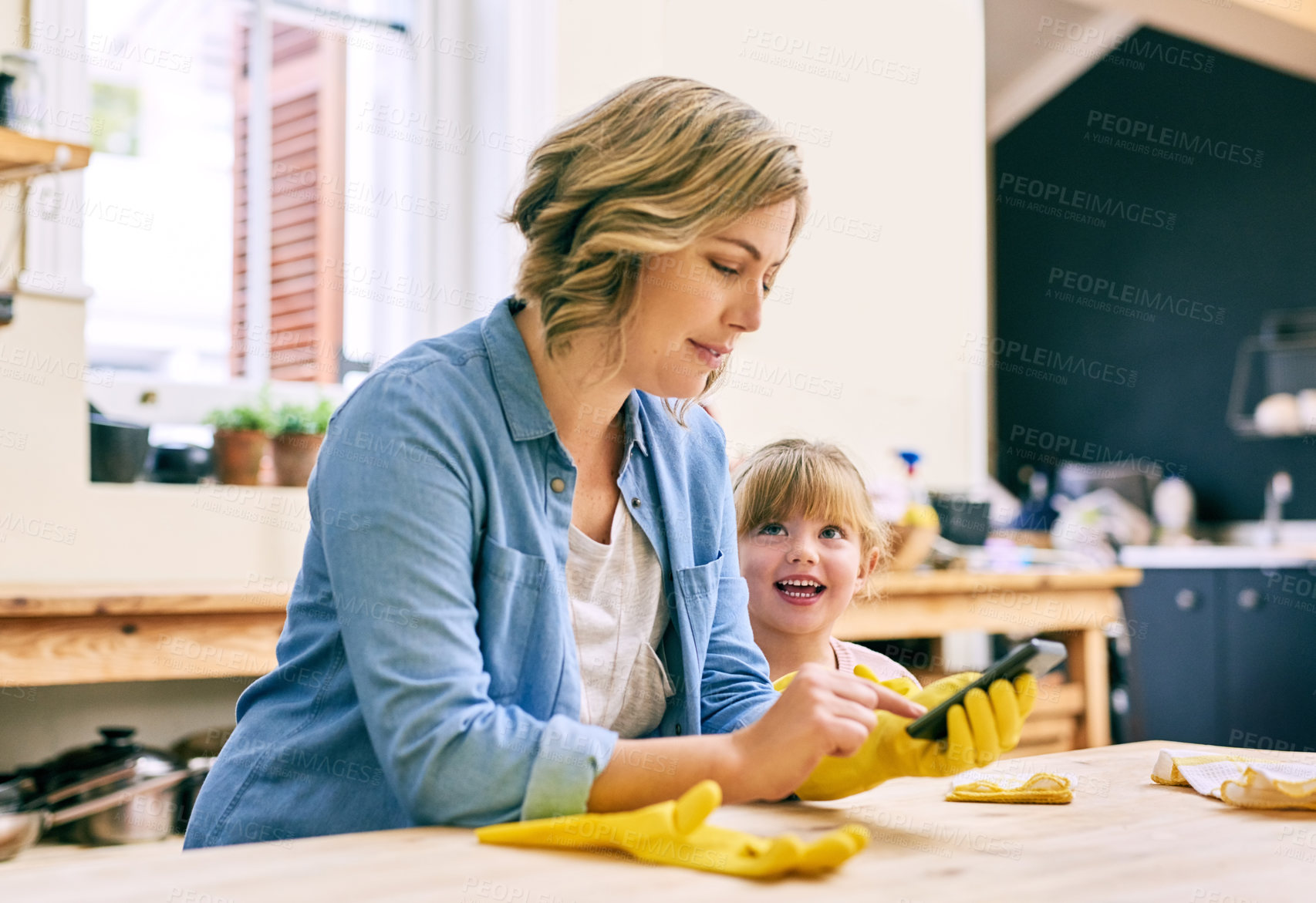 Buy stock photo Shot of a focused young mother typing on her mobile phone while her young little daughter stands beside her