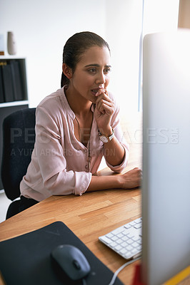 Buy stock photo Shot of a young businesswoman biting her nails while working on a computer in an office