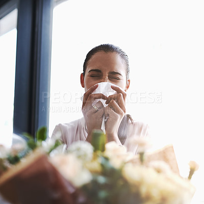 Buy stock photo Shot of a young businesswoman blowing her nose in front of a bouquet of flowers